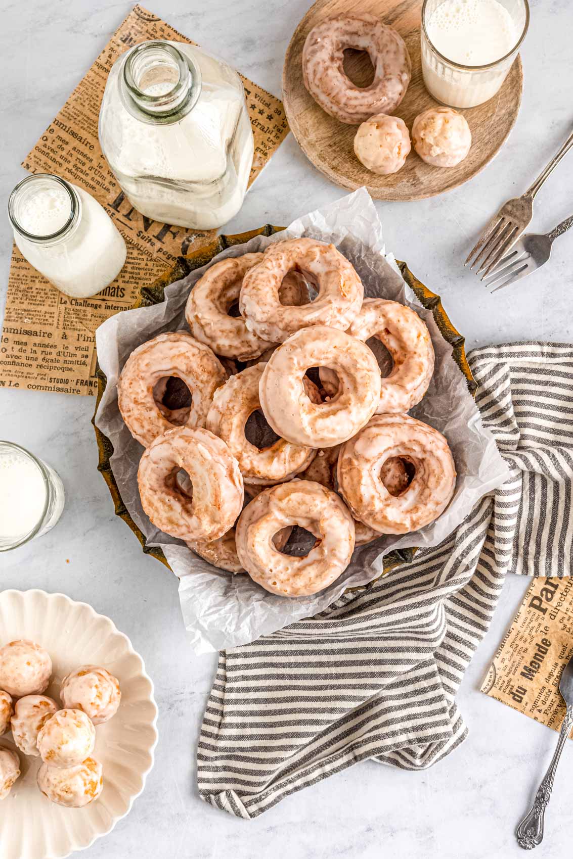 pan filled with several old-fashioned sour cream donuts on parchment paper and a kitchen linen next to a glass of milk