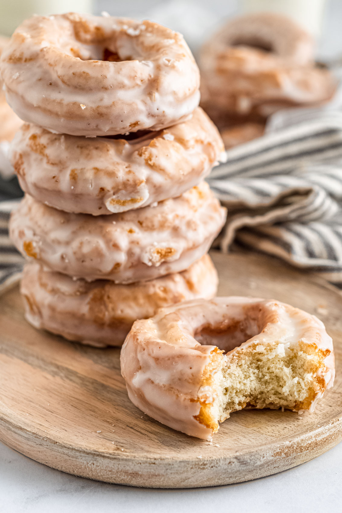 stack of old-fashioned sour cream donuts with a kitchen linen next to a striped linen; one donut has a large bite taken out