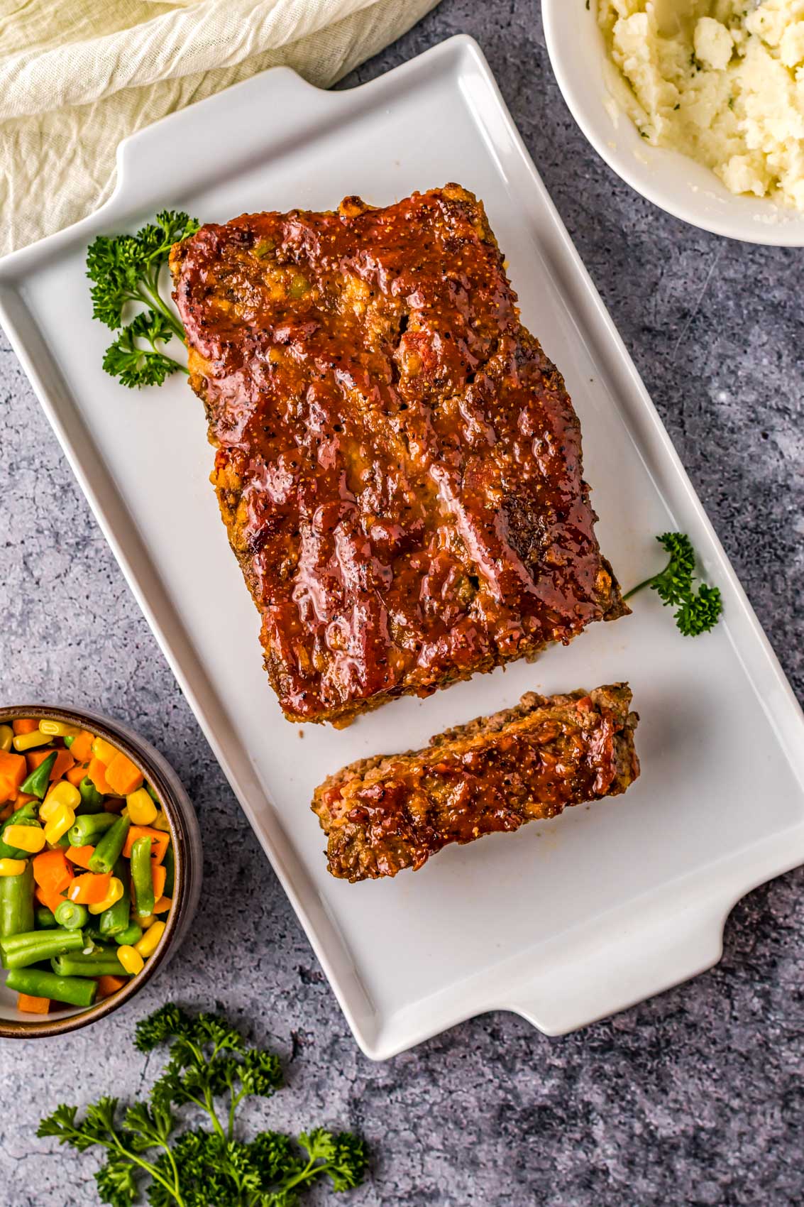 thick, juicy meatloaf on a platter with parsley and veggies