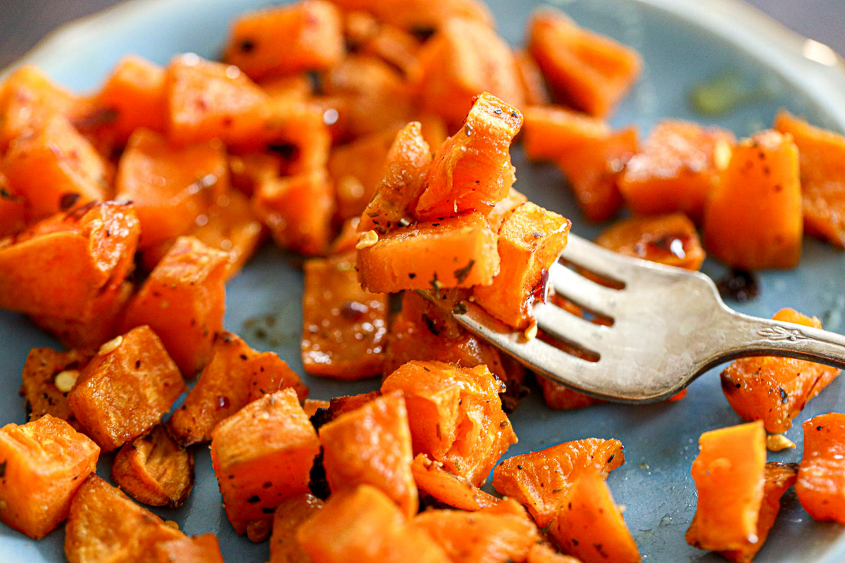 cubed sweet potatoes on a fork with pepper flakes as seasoning
