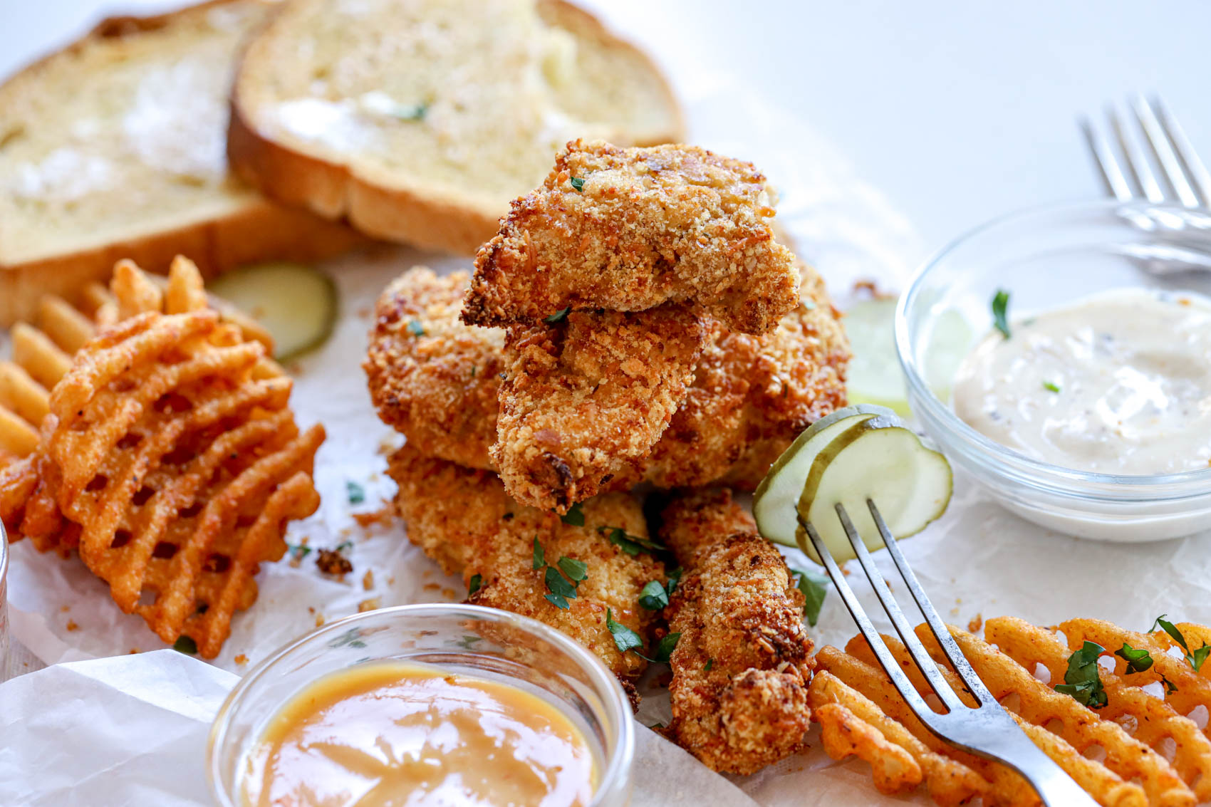 chicken tenders next to dipping sauce, waffle fries and pickles