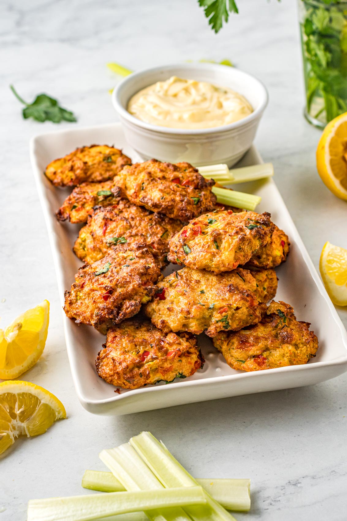 a dozen crab cakes on a large platter with lemon wedges and tartar sauxe