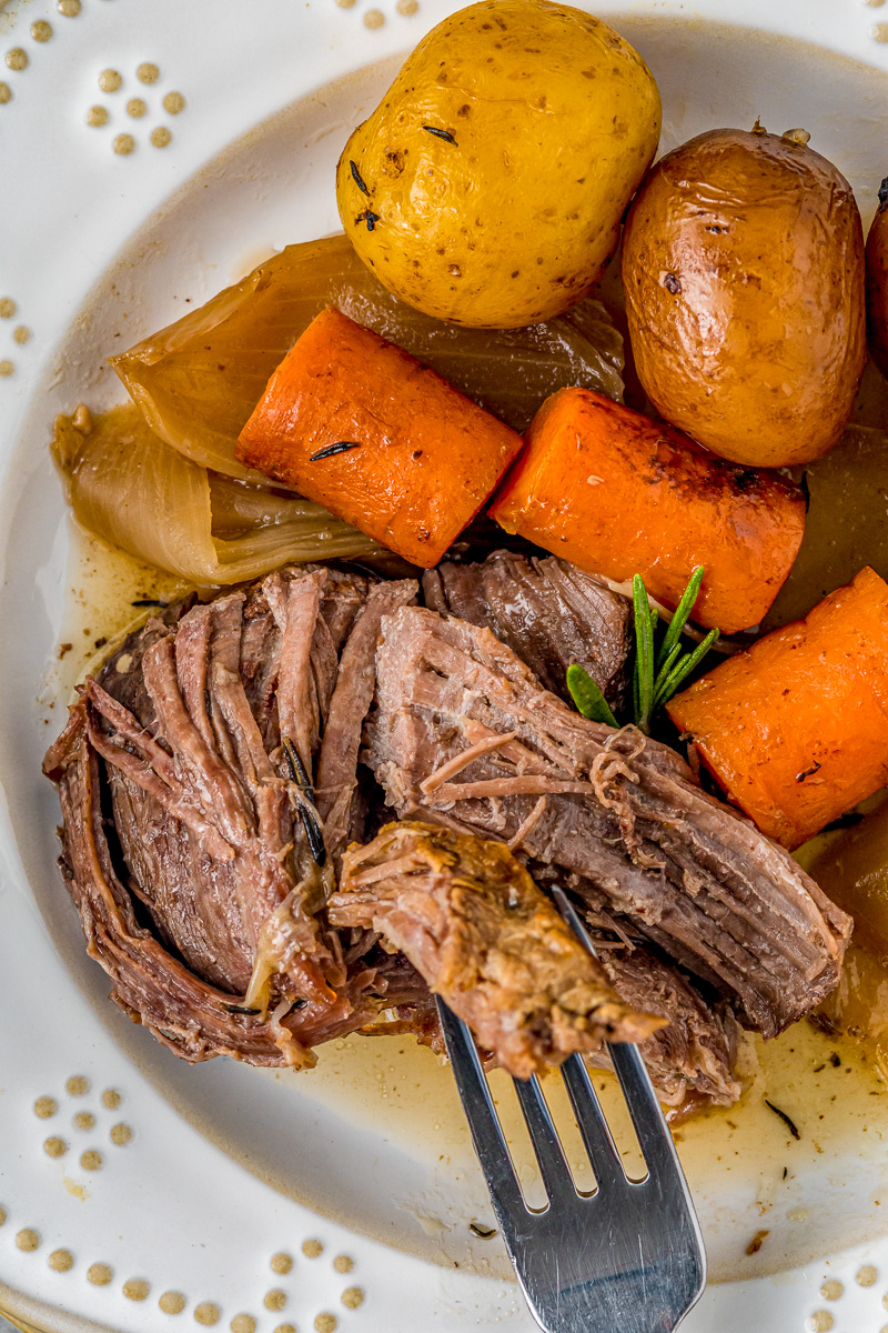 roast, carrots, onion and potatoes on a plate with fork