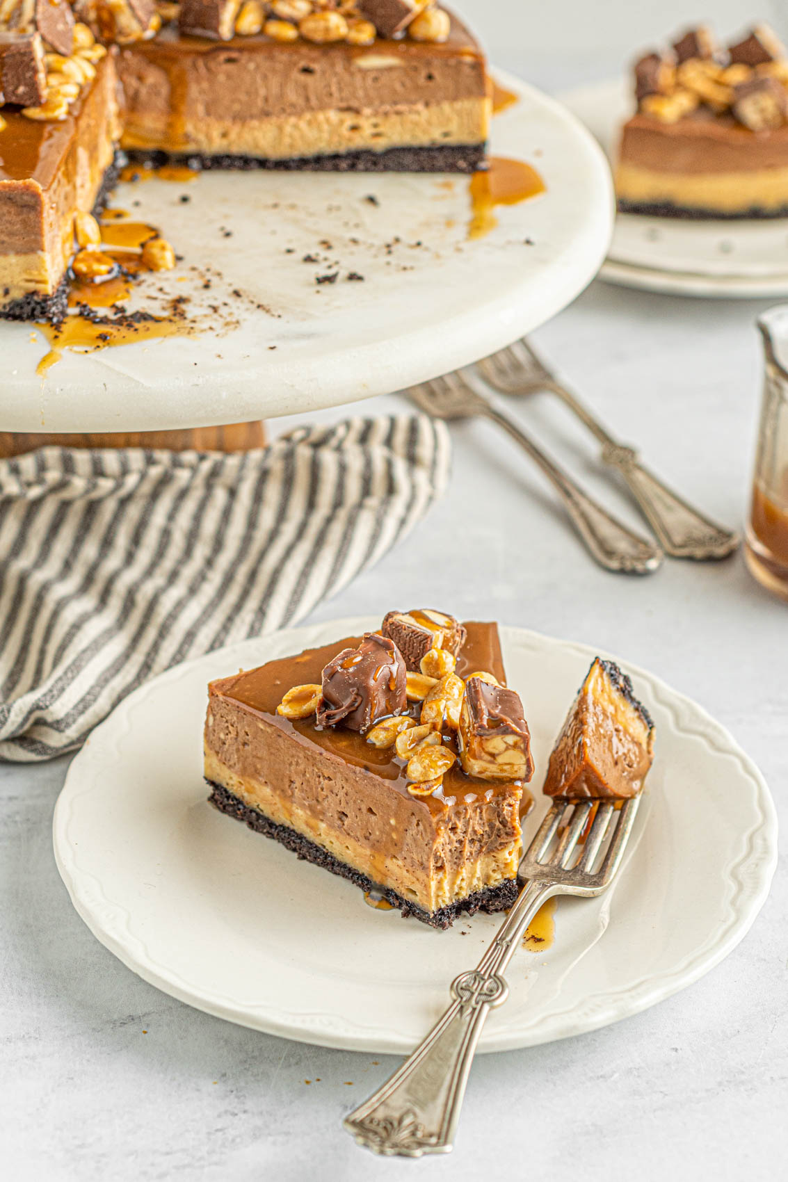 snickers cheesecake slice with fork on a plate next to linen
