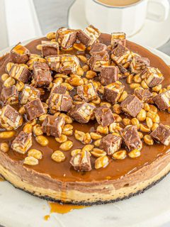snickers cheesecake with bits of candy bar on top covered in caramel