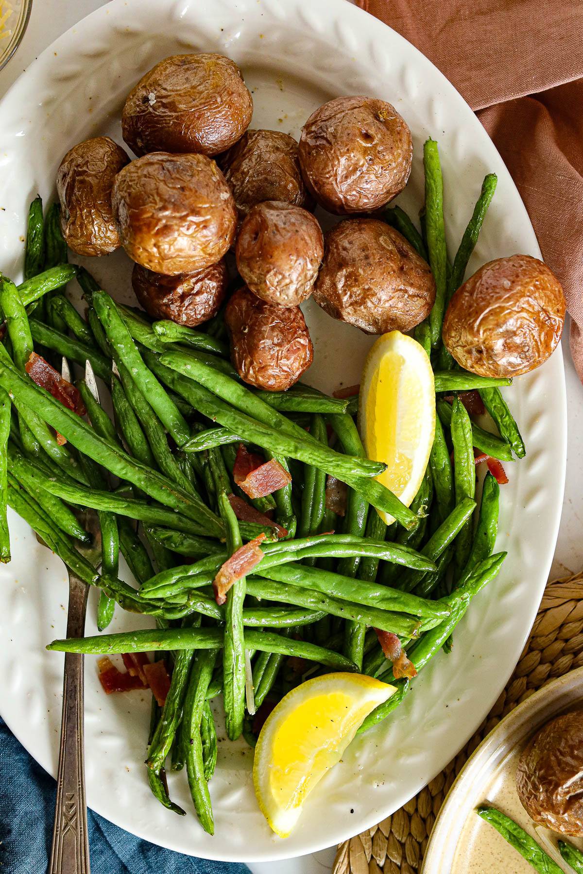 platter with green beans with bacon bits, potatoes, and lemon wedges
