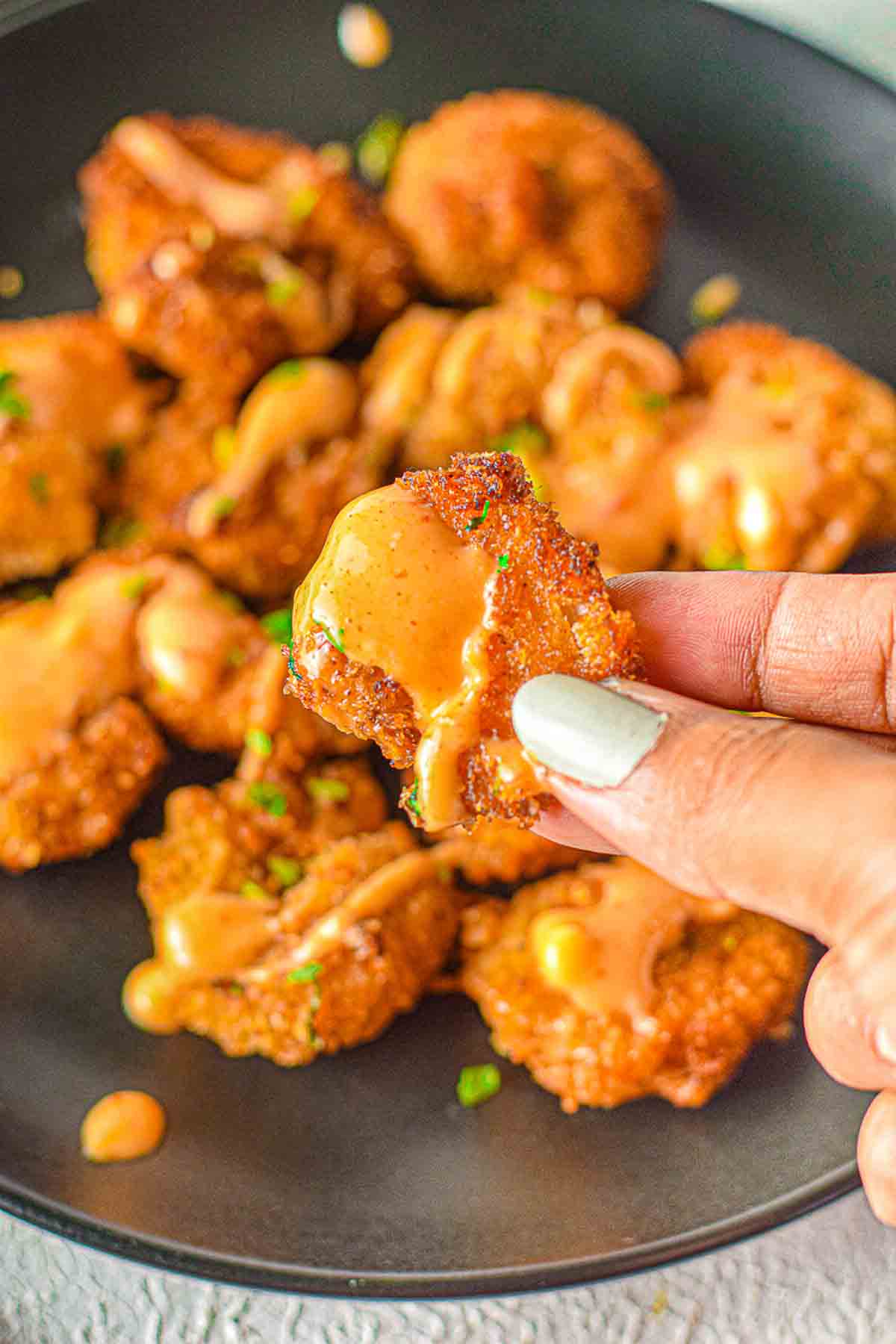 hand holding a shrimp covered in creamy, spicy bang bang sauce