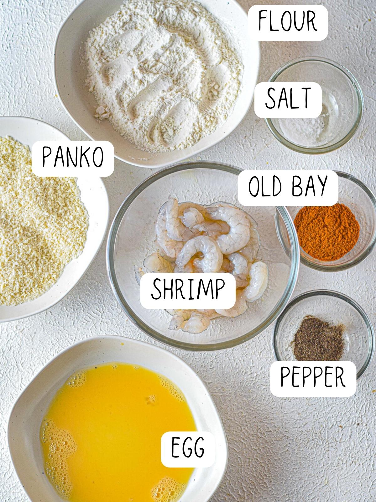 ingredients for crispy bang bang shrimp, including pepper, old bay, egg wash, panko and flour