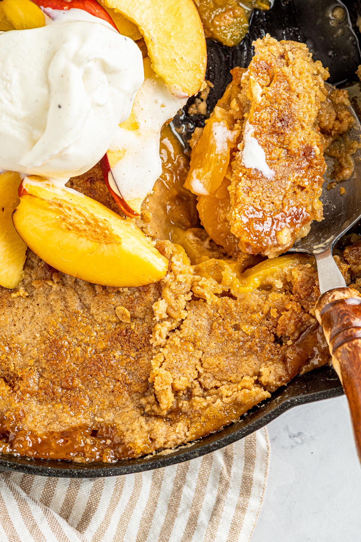 large wooden handled spoon scooping out cobbler from a cast iron skillet