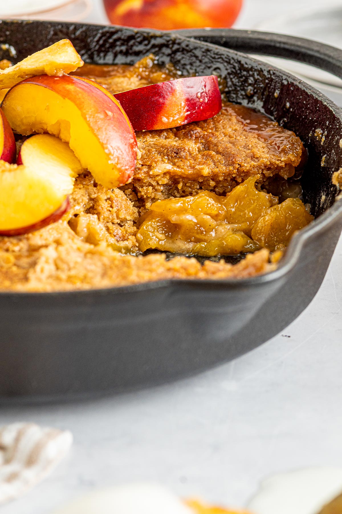 peach cobbler in a cast iron skillet covered with fresh peaches