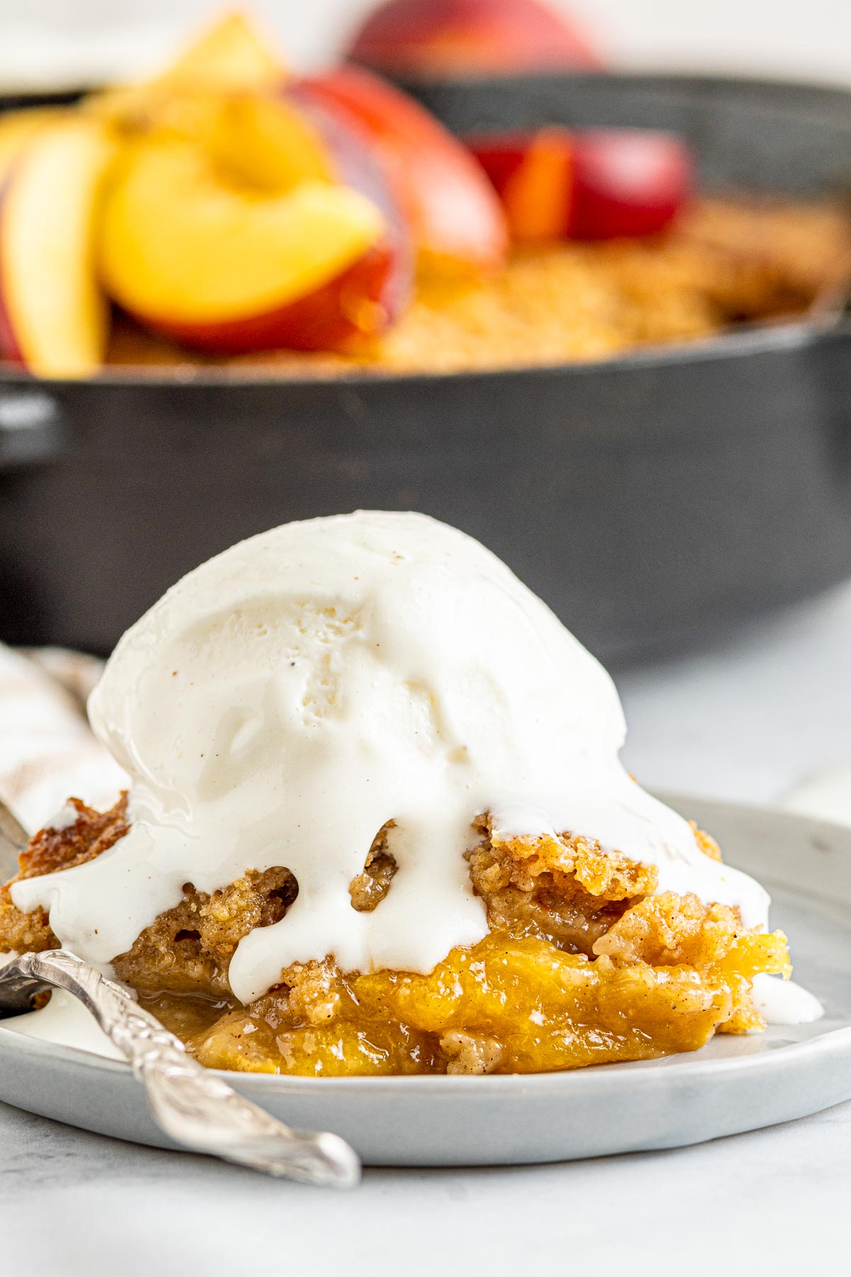 large scoop of vanilla ice cream on top of peach cobbler