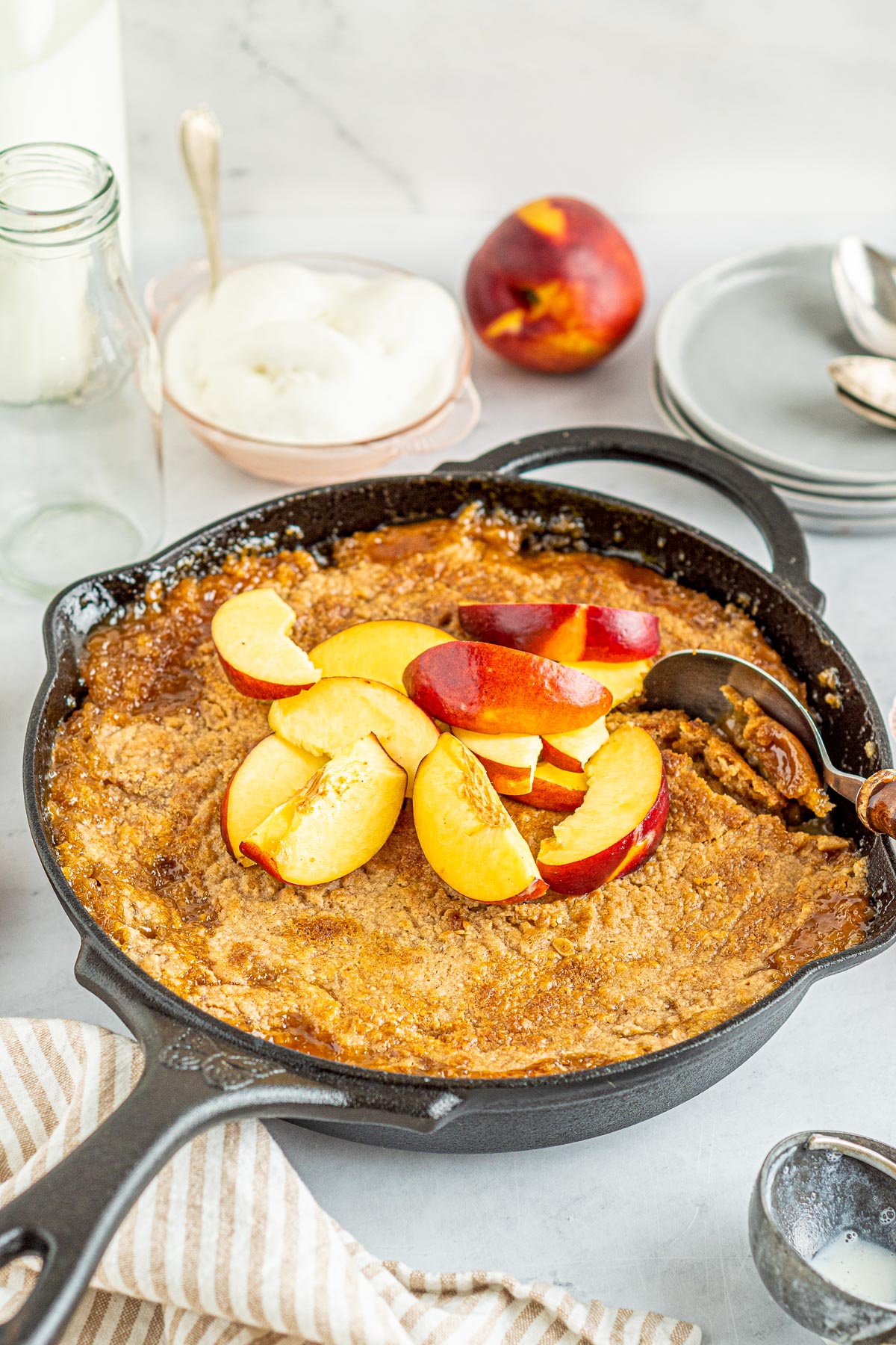 peach cobbler with ice cream, plates, spoons, and fresh peaches