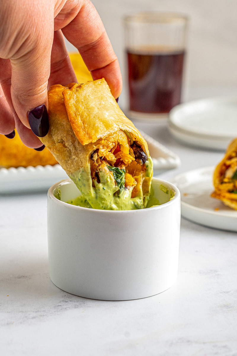 fried southwest egg roll with spinach, corn, black beans, and red peppers being dipped into avocado ranch sauce