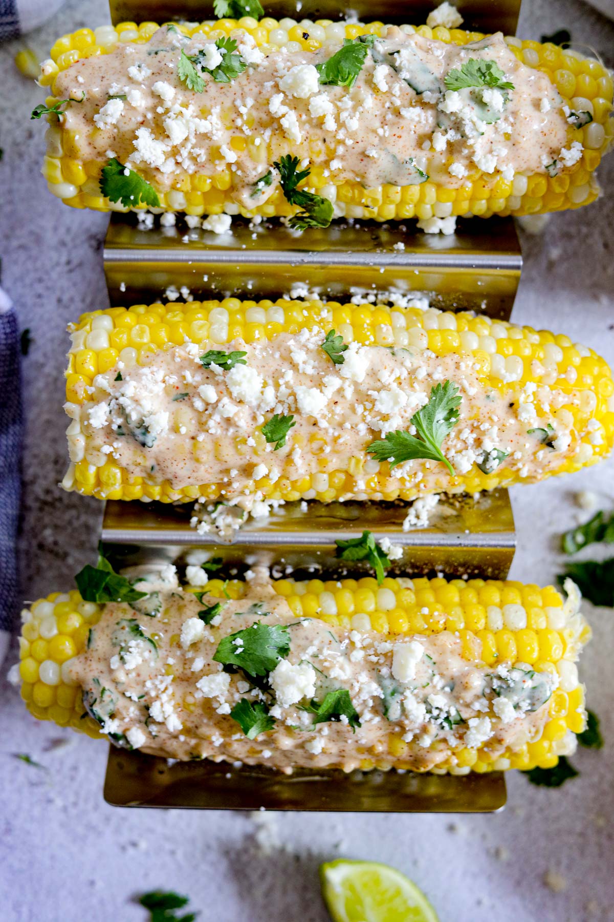 three ears of corn with cream sauce, cilantro and crumbled cheese