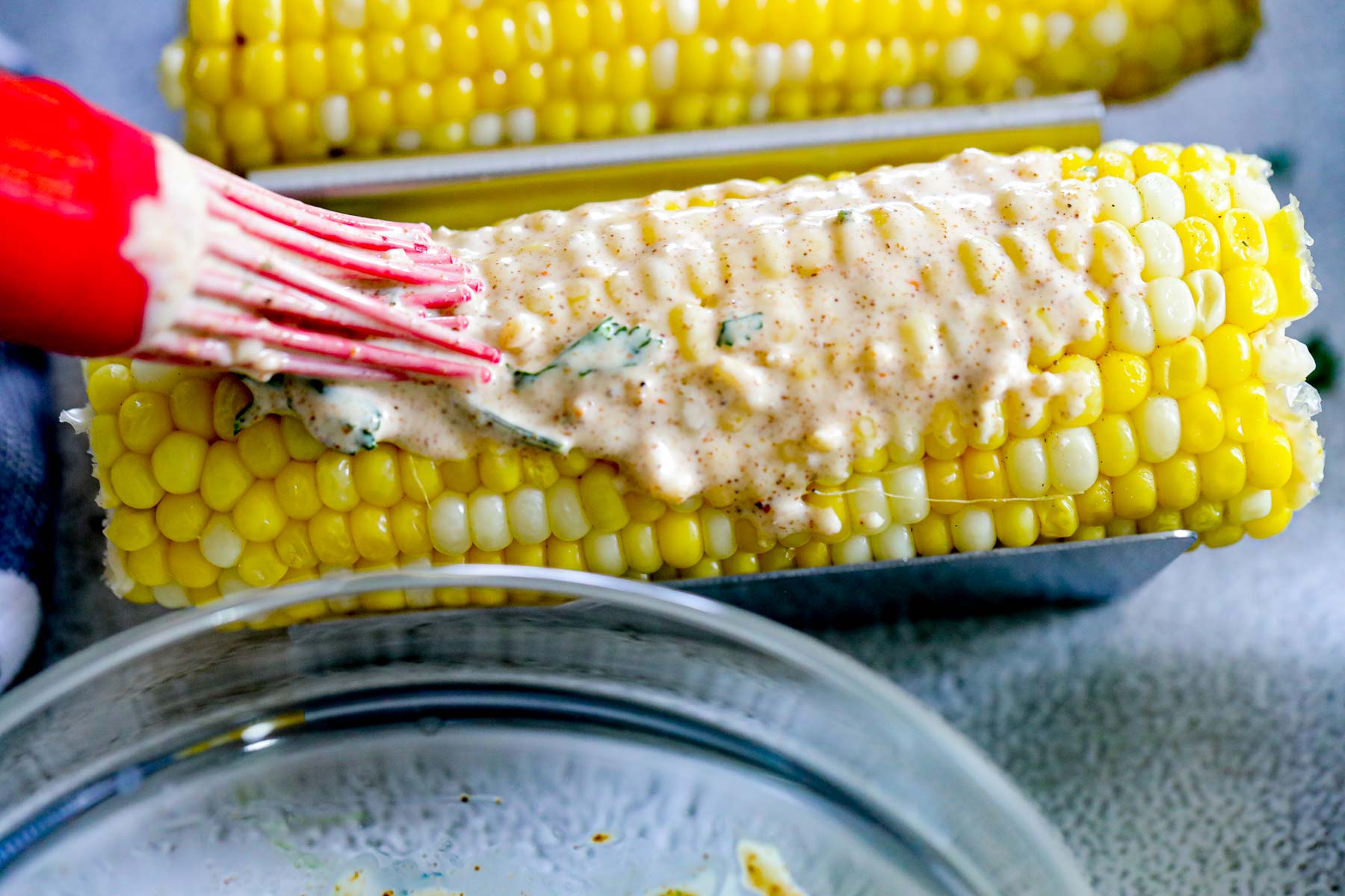 brushing on tangy cream sauce on an ear of yellow corn