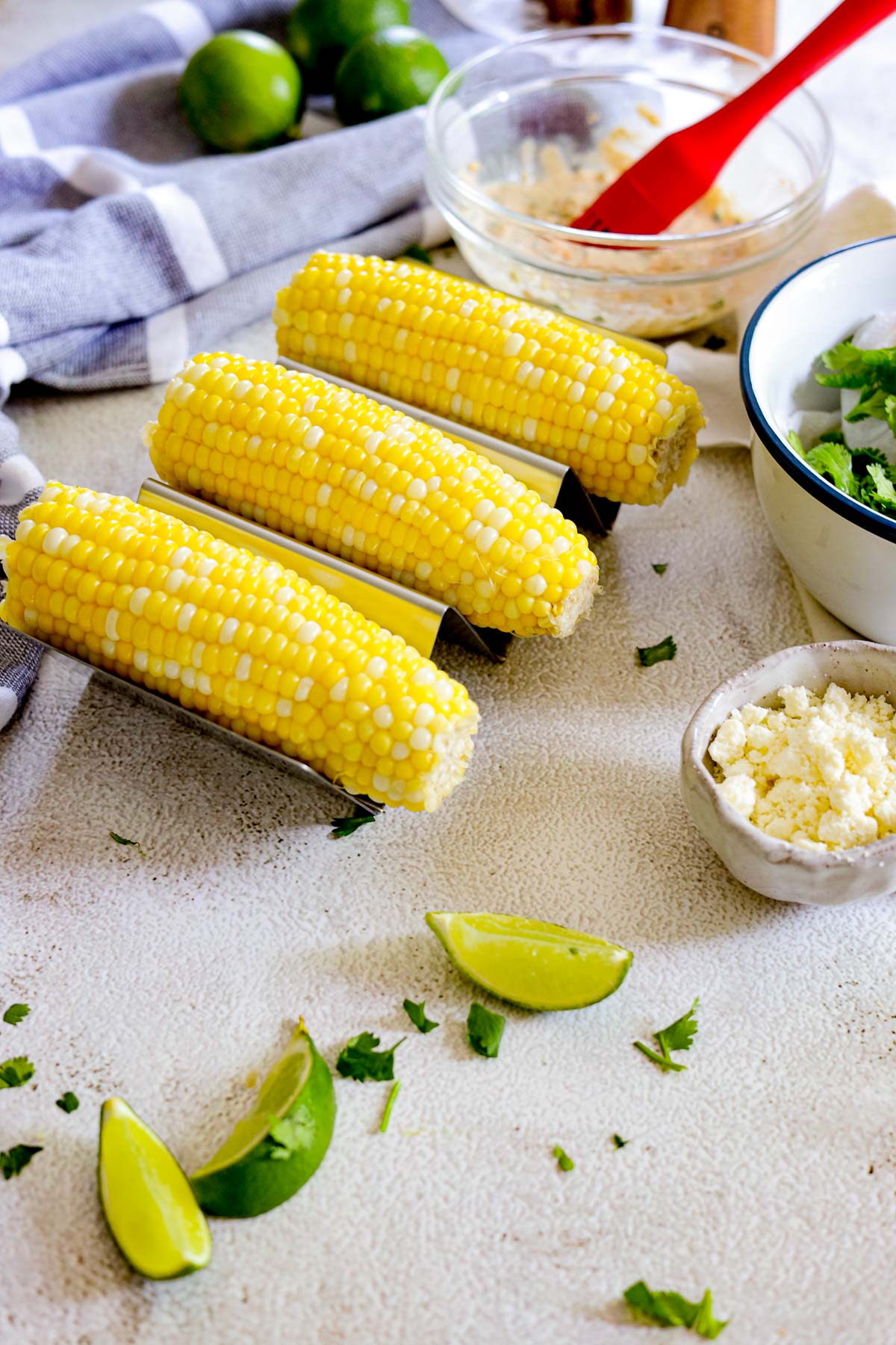 corn with a bowl of cilantro and cotija cheese next to lime wedges
