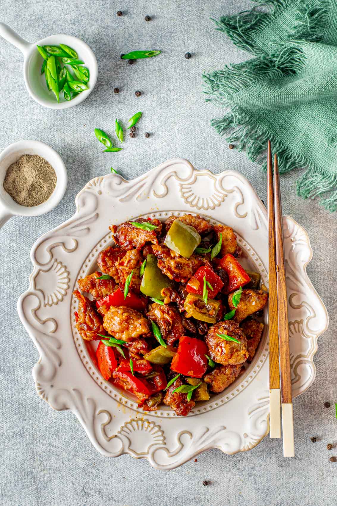 sticky pepper chicken with chopsticks on a plate with fried red and green peppers