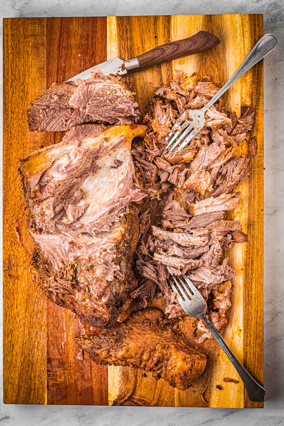 shredding pork butt on a wooden cutting board with two forks