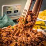 slow cooker pork butt being lifted with tongs