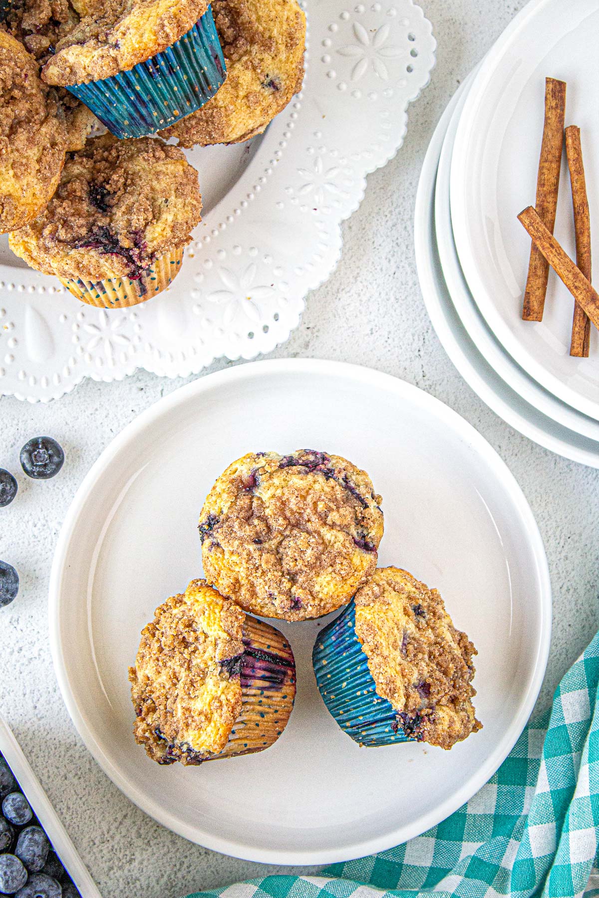 three blueberry streusel muffins on a white plate with cinnamon sticks and blueberries around