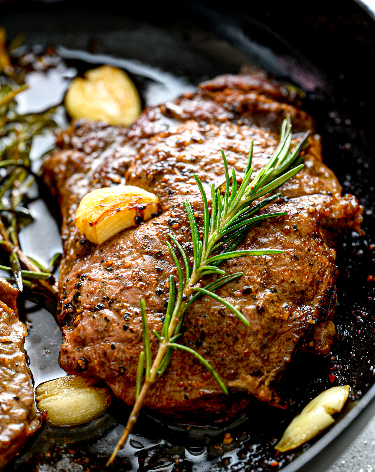 steak with rosemary and garlic cloves in a cast iron pan