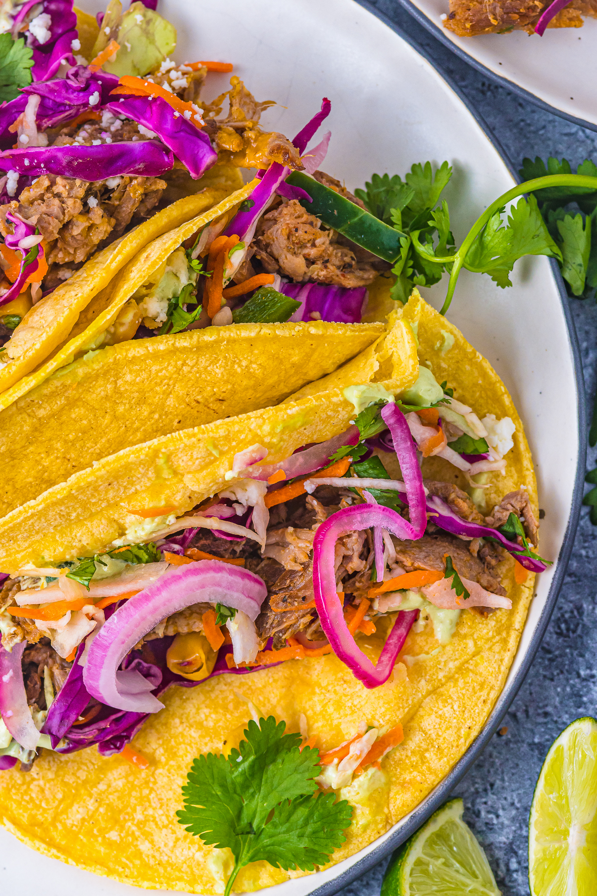 corn tortilla with carnitas and pickled onions, topped with cilantro garnish next to lime wedges