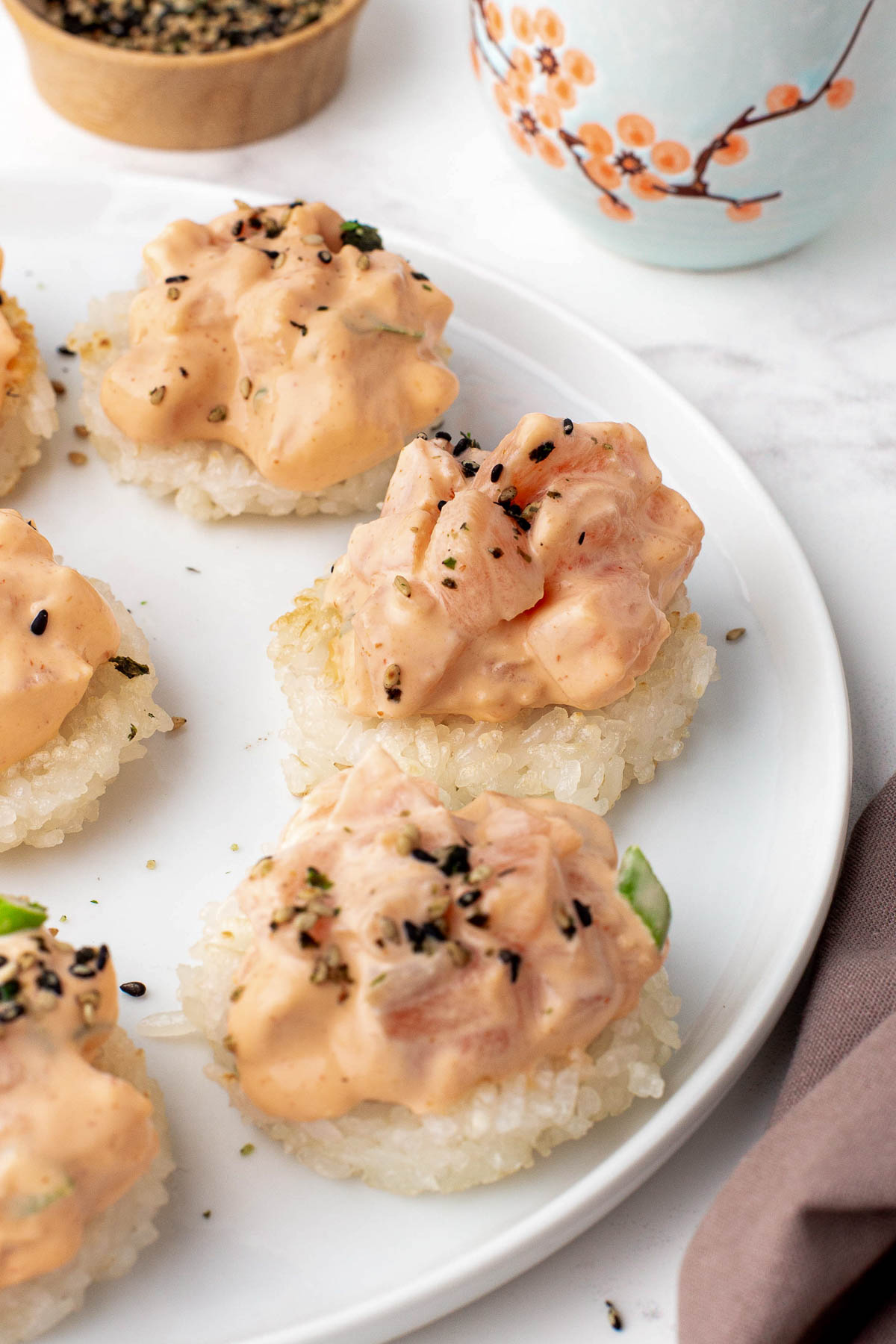 salmon sushi bites on a white plate with tiny rice cakes and sesame seeds for garnish