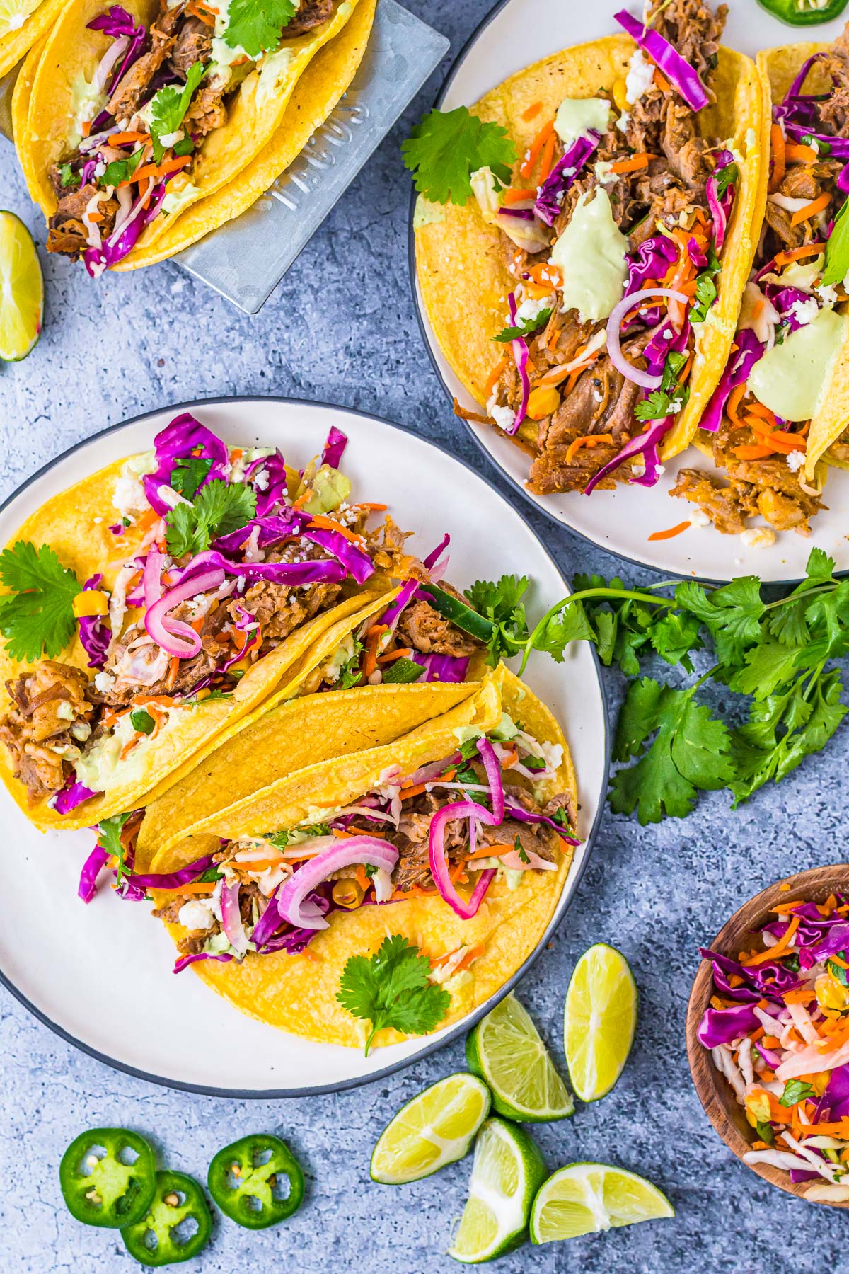 two plates full of tacos with slaw, lime, pickled onion, cilantro, and pulled pork