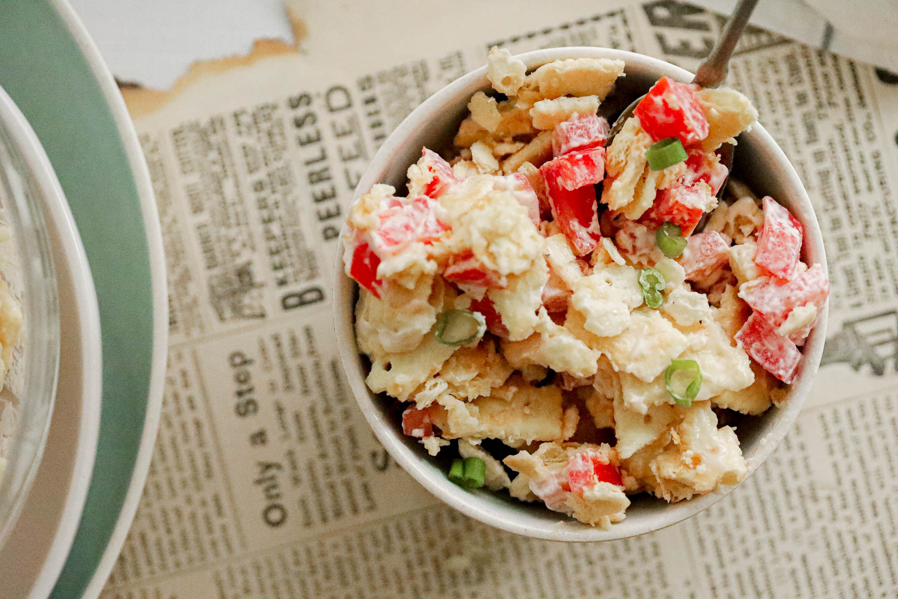 bowl of mayo cracker salad with tomatoes next to a newspaper